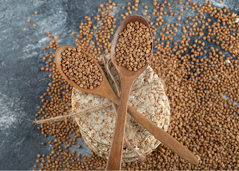 Two wooden spoons of raw buckwheat and crispbread on marble surface. High quality photo