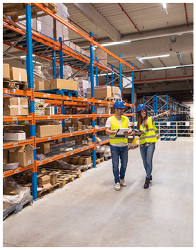 Two caucasian warehouse workers walking in distribution storage area discussing about logistics and organization.